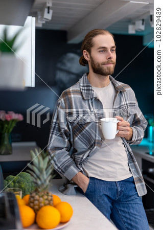 Man enjoying morning coffee in kitchen with modern interior, drinking fresh warm beverage at home. 102829489