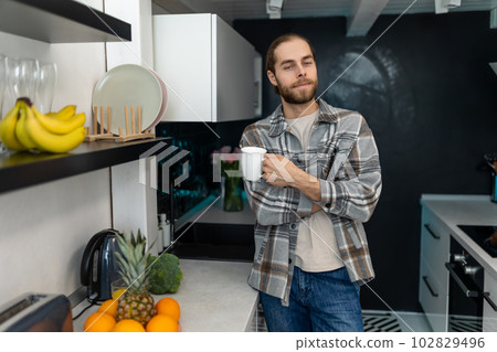 Man enjoying morning coffee in kitchen with modern interior, drinking fresh warm beverage at home. 102829496