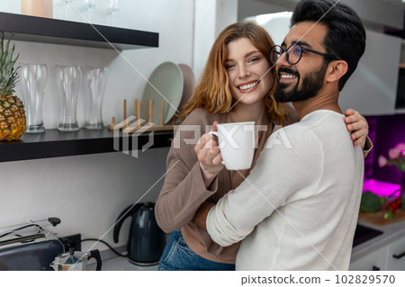 Woman drinking coffee with man and hugging while sitting on kitchen counter. Woman drinking coffee with man and hugging while sitting on kitchen counter. 102829570