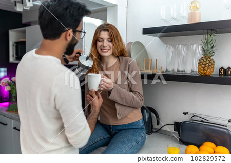 Woman drinking coffee with man while sitting on kitchen counter. 102829572