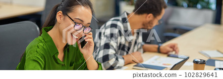 Young cheerful asian woman talking by phone and making some notes while working in the modern office Young cheerful asian woman talking by phone and making some notes while working in the modern office 102829641