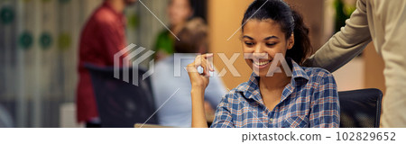 Young cheerful caucasian man helping female coworker with computer work, two young multiracial colleagues using laptop and discussing project Young cheerful caucasian man helping female coworker with computer work, two young multiracial colleagues using laptop and discussing project 102829652
