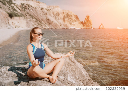 Woman sea yoga. Happy woman meditating in yoga pose on the beach, ocean and rock mountains. Motivation and inspirational fit and exercising. Healthy lifestyle outdoors in nature, fitness concept. 102829939