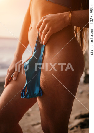 Woman summer travel sea. Happy tourist enjoy taking picture outdoors for memories. Woman traveler posing on the beach at sea, holding a bikini bottom in her hand, sharing travel adventure journey 102829993
