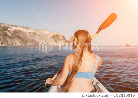 Woman in kayak back view. Happy young woman with long hair floating in kayak on calm sea. Summer holiday vacation and cheerful female people relaxing having fun on the boat. Woman in kayak back view. Happy young woman with long hair floating in kayak on calm sea. Summer holiday vacation and cheerful female people relaxing having fun on the boat. 102830019