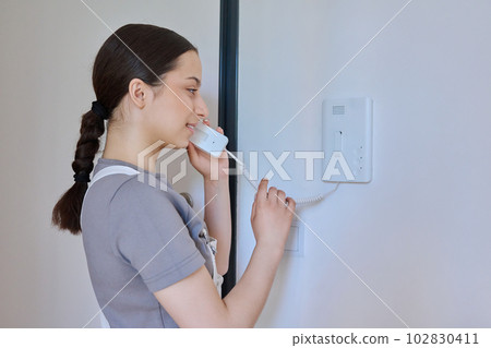 Teenage girl holding intercom handset while talking to guest Teenage girl holding intercom handset while talking to guest 102830411