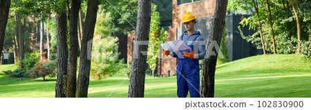 Full length of young builder standing outdoors with blueprint while working on cottage construction Full length of young builder standing outdoors with blueprint while working on cottage construction 102830900