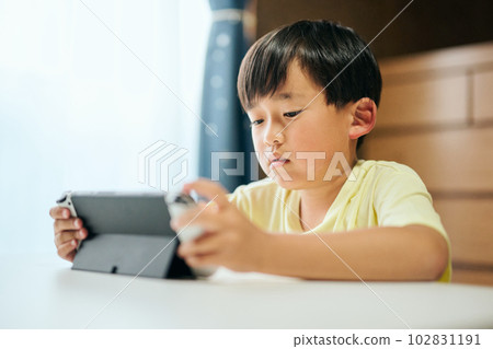 Elementary school boy playing a game on a home video game console 102831191