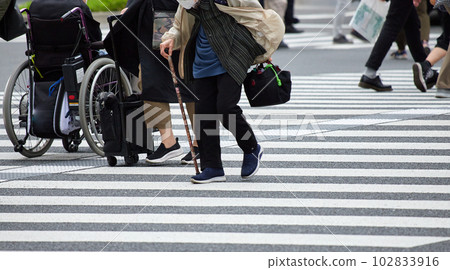 A senior woman crossing a pedestrian crossing and a disabled person in a wheelchair A senior woman crossing a pedestrian crossing and a disabled person in a wheelchair 102833916