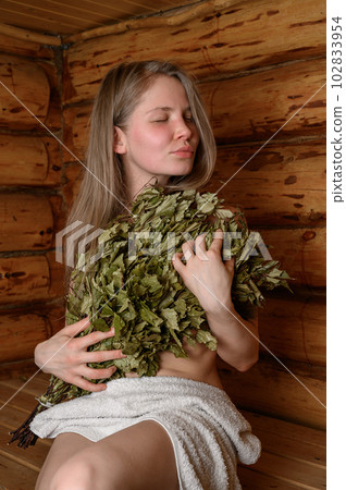 Young woman relaxing in a sauna dressed in a towel and birch broom Young woman relaxing in a sauna dressed in a towel and birch broom 102833954