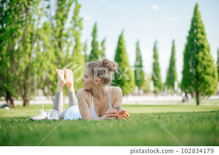 Attractive sportive girl lies on the grass and relaxes in park Attractive sportive girl lies on the grass and relaxes in park 102834179