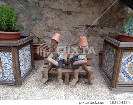 Wooden dolls sitting on a wooden bench. Surrounded by pots. In Medinaceli, in Soria. Photography. 102834384