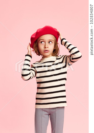 Portrait of beautiful, stylish little girl, child in red beret and striped sweater against pink studio background. Parisian style 102834807