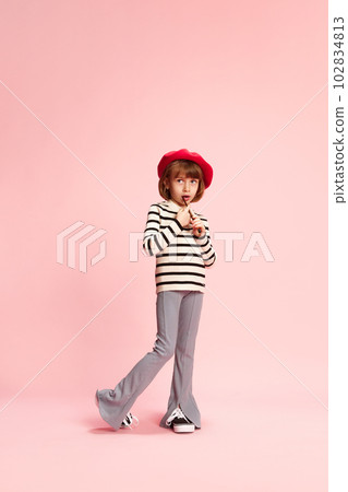 Full-length portrait of little girl, child in red beret and striped sweater posing with painting brush against pink studio background 102834813