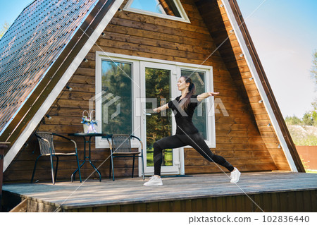 Active woman in sport clothing does sports on terrace of country house 102836440
