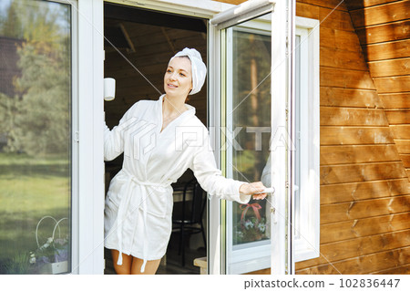 Beautiful woman in bathrobe opened door of her log cabin and looks out 102836447