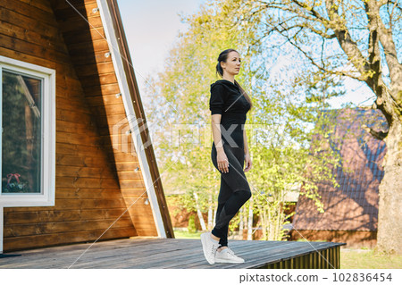 Concentrated woman in tracksuit went out on terrace of wooden house in morning 102836454