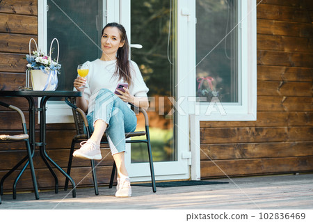 Cheerful woman relaxing on wooden cottage on the terrace in nature Cheerful woman relaxing on wooden cottage on the terrace in nature 102836469