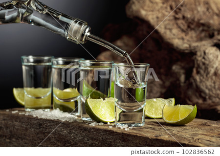 Tequila is poured from a bottle into a glass. 102836562