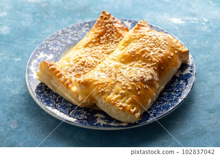 Puff pastry dough. Folded baked puff pastry pie in a plate, blue background Puff pastry dough. Folded baked puff pastry pie in a plate, blue background 102837042