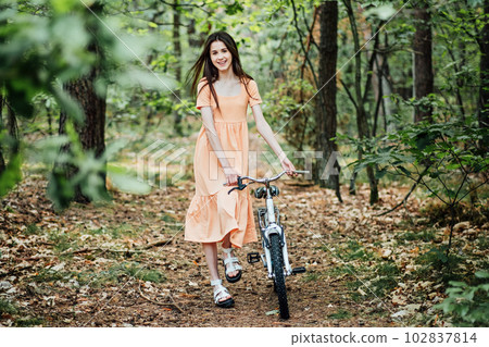 Walk in the woods for wellness, Health benefits of forests. Immerse Yourself in a Forest. A young girl rolls a bicycle along a forest path in tree wood Walk in the woods for wellness, Health benefits of forests. Immerse Yourself in a Forest. A young girl rolls a bicycle along a forest path in tree wood 102837814