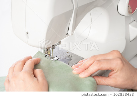Female hands stitching white fabric on modern sewing machine at workplace in atelier Female hands stitching white fabric on modern sewing machine at workplace in atelier 102838458