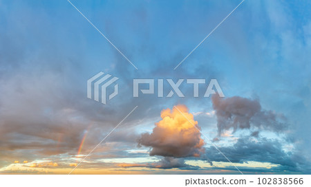 Rainbow and fluffy clouds at sunset after the rain. 102838566