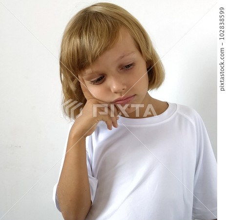 Little disappointed girl 6-7 years old with blond hair, white background. Tanned skin. White T-shirt. Copy space. The girl raised her right hand and put her index finger to her temple. Hairstyle Bob. Little disappointed girl 6-7 years old with blond hair, white background. Tanned skin. White T-shirt. Copy space. The girl raised her right hand and put her index finger to her temple. Hairstyle Bob. 102838599