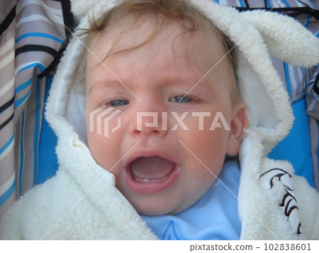 Crying baby. A lovely little boy in a white overalls is sitting in a stroller. Children's whims and grimaces. White and blue colors for clothes and a stroller. Caucasian emotional child Crying baby. A lovely little boy in a white overalls is sitting in a stroller. Children's whims and grimaces. White and blue colors for clothes and a stroller. Caucasian emotional child 102838601