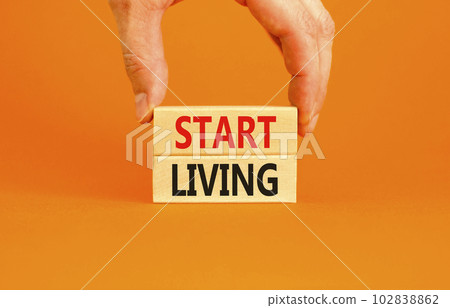 Start living symbol. Concept words Start living on beautiful wooden block. Beautiful orange table orange background. Businessman hand. Business and Start living concept. Copy space. Start living symbol. Concept words Start living on beautiful wooden block. Beautiful orange table orange background. Businessman hand. Business and Start living concept. Copy space. 102838862