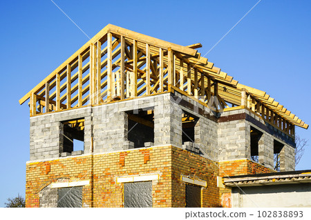 Unfinished residential house with brick and block walls and a wooden beam roof structure 102838893
