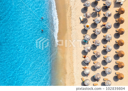 Aerial view of colorful umbrellas on sandy beach, people in blue sea Aerial view of colorful umbrellas on sandy beach, people in blue sea 102839804