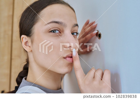 Young teenage female looking through peephole on front door 102839838
