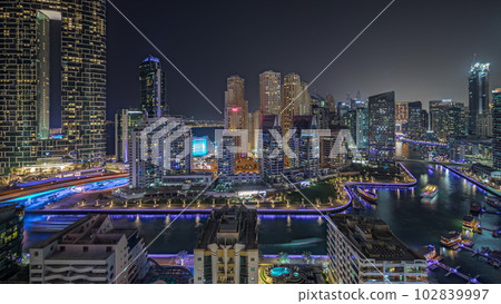 Panorama showing Dubai Marina with several boat and yachts parked in harbor and skyscrapers around canal aerial night timelapse. 102839997