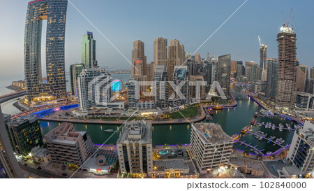 Panoramic view of Dubai Marina with several boat and yachts parked in harbor and skyscrapers around canal aerial day to night timelapse. 102840000