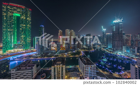 Dubai Marina with several boat and yachts parked in harbor and skyscrapers around canal aerial all night timelapse. 102840002