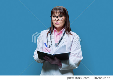 Female doctor taking note information in notebook on blue background Female doctor taking note information in notebook on blue background 102840366