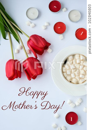 Text HAPPY MOTHERS DAY greeting card. Red tulips candles White cup of cacao coffee marshmallows morning breakfast. Holiday background. Top view Flat lay Saying 102840803