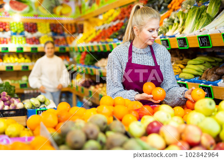 Focused saleswoman arranging oranges on shelves in greengrocery store Focused saleswoman arranging oranges on shelves in greengrocery store 102842964