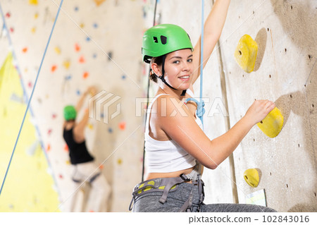 Positive extreme young woman with rope training on concrete climbing rock wall to maintain healthy discipline in indoor adventure park Positive extreme young woman with rope training on concrete climbing rock wall to maintain healthy discipline in indoor adventure park 102843016