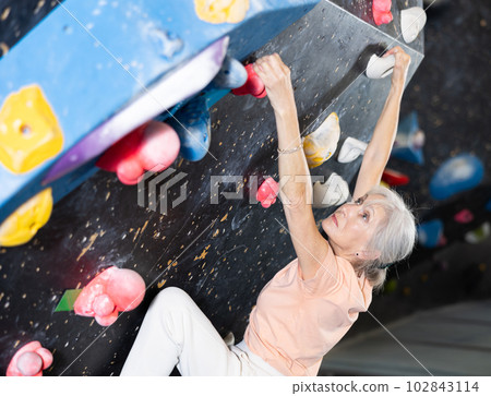 Confident mature woman scaling artificial climbing wall in climbing gym Confident mature woman scaling artificial climbing wall in climbing gym 102843114