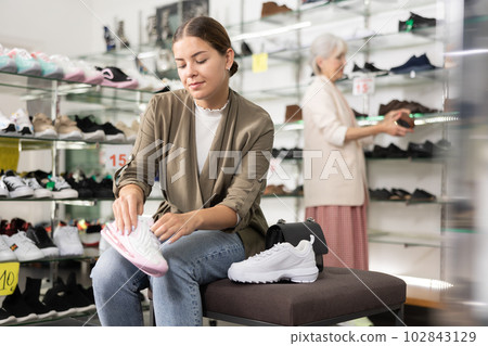 Young woman trying on sneakers in shoe store 102843129