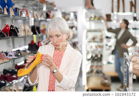Mature female client is inspecting ballet flats in shoe bounique Mature female client is inspecting ballet flats in shoe bounique 102843172