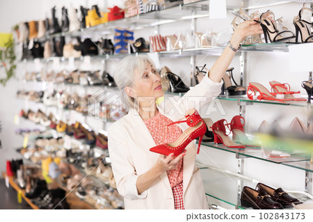 Granny choosing shoes while standing in salesroom of shoeshop 102843173