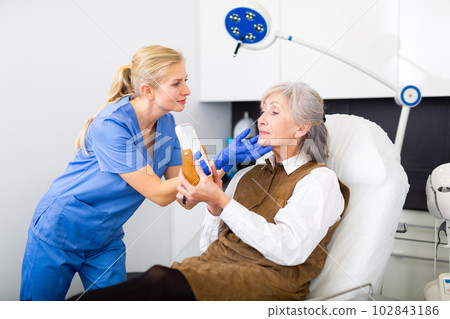 Cosmetologist explaining future facial procedure to elderly female patient 102843186