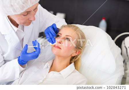 Cosmetologist doing botulotoxin injections for young woman Cosmetologist doing botulotoxin injections for young woman 102843271
