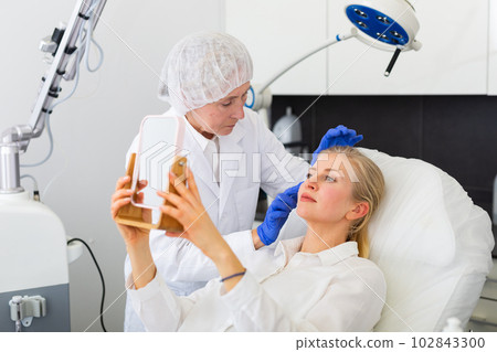 Young woman and cosmetologist looking in mirror 102843300