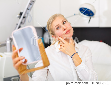 Happy woman examining her face after cosmetology procedures in clinic 102843305
