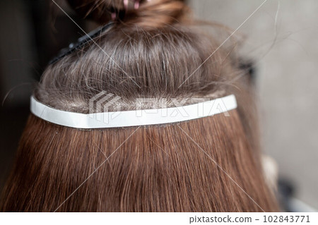 Hair ribbons for extensions on a woman's head at home. Hair ribbons for extensions on a woman's head at home. 102843771
