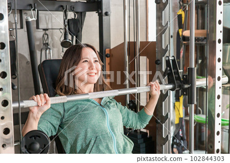 A smiling Japanese woman doing muscle training using a shoulder press machine at the gym A smiling Japanese woman doing muscle training using a shoulder press machine at the gym 102844303